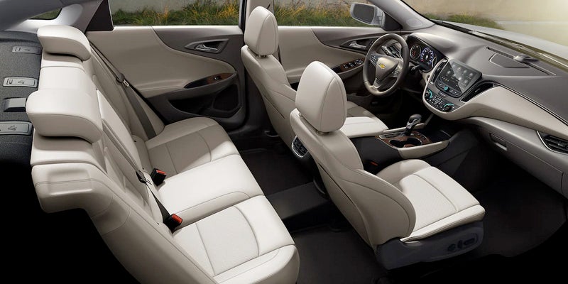 Interior of a car with light beige leather seats, dark floor mats, and an infotainment system screen on the dashboard.