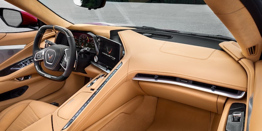 Interior of a Chevrolet Corvette with tan leather and black accents, including a digital display and carbon fiber steering wheel.