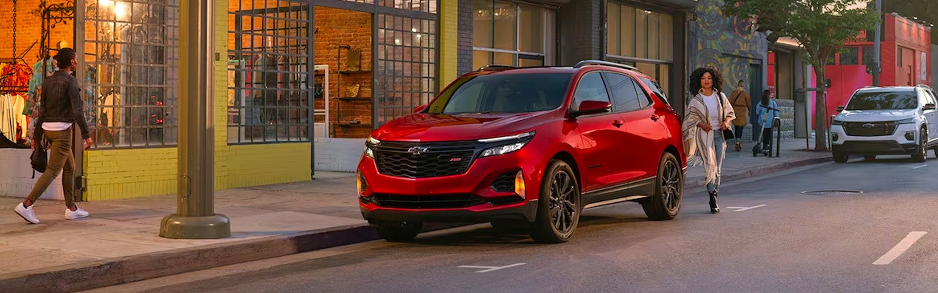 A red Chevy Equinox parked on a street with pedestrians and another white Chevy in an urban setting.