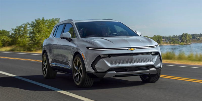 Silver Chevrolet SUV driving near a lake on an open road