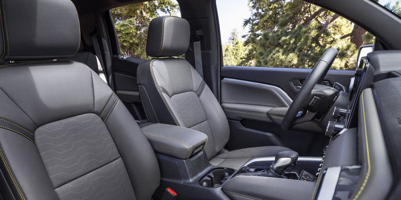 Part of a car's interior features two-tone gray bucket seats with yellow stitching and textured inserts.