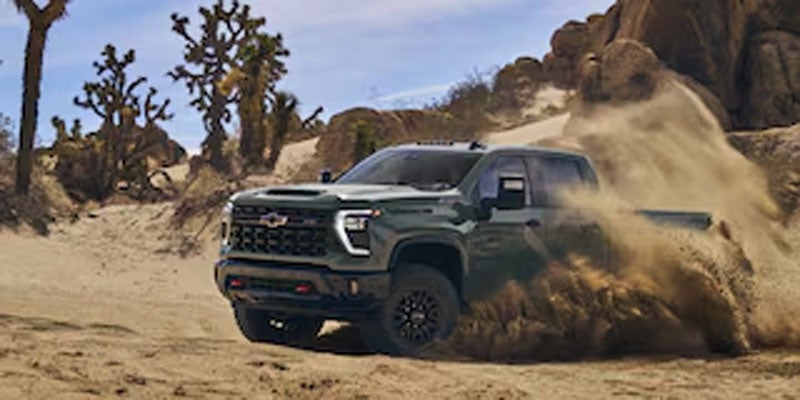 A dark green Chevrolet pickup truck driving fast through a sandy desert