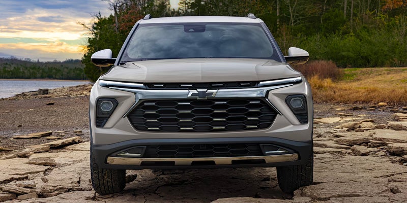 Rear view of a light brown Chevrolet Trailblazer ACTIV SUV parked on a rocky shoreline next to a lake.