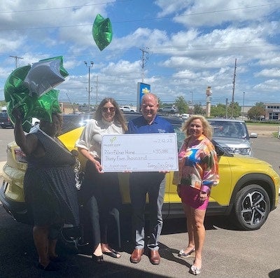 Four people pose with an oversized check for $35,000, green and white balloons, and a yellow SUV.