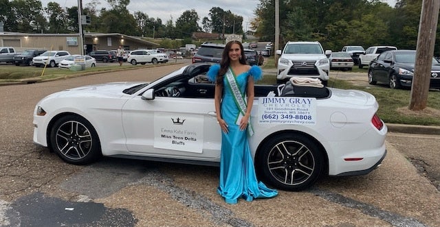 Emma Kate Forms, Miss Teen Delta Bluffs, in a turquoise gown and crown, stands beside a white convertible.