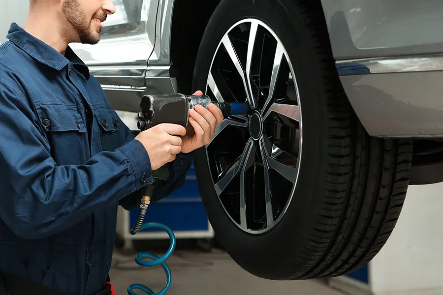 A mechanic uses a pneumatic impact wrench to tighten a car wheel