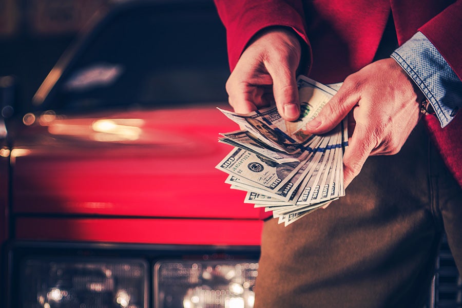 A person in a red jacket holding a large fan of cash